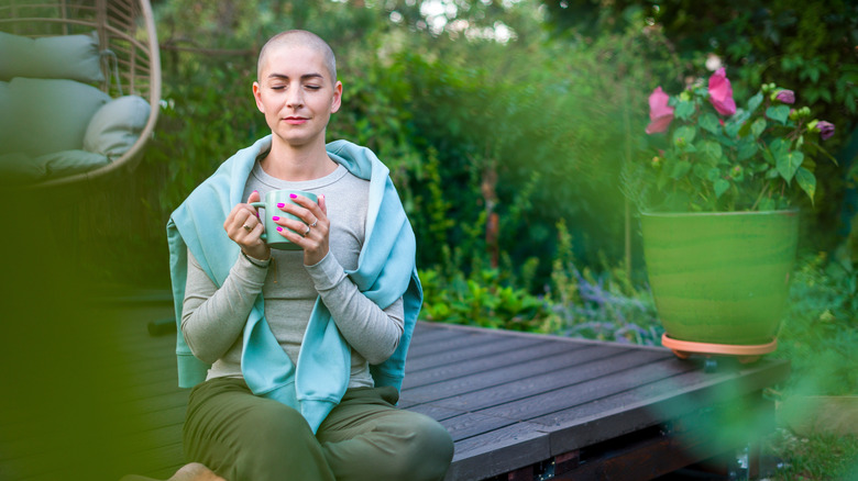 A young woman enjoys a coffee on an outside deck surrounded by greenery