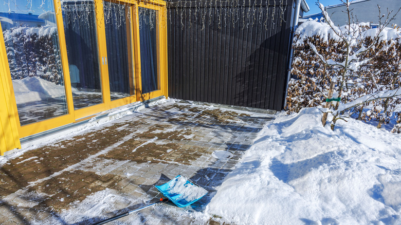 snow shovel rests on a cleared brick patio