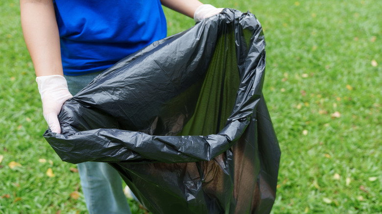 Holding black garbage bag open