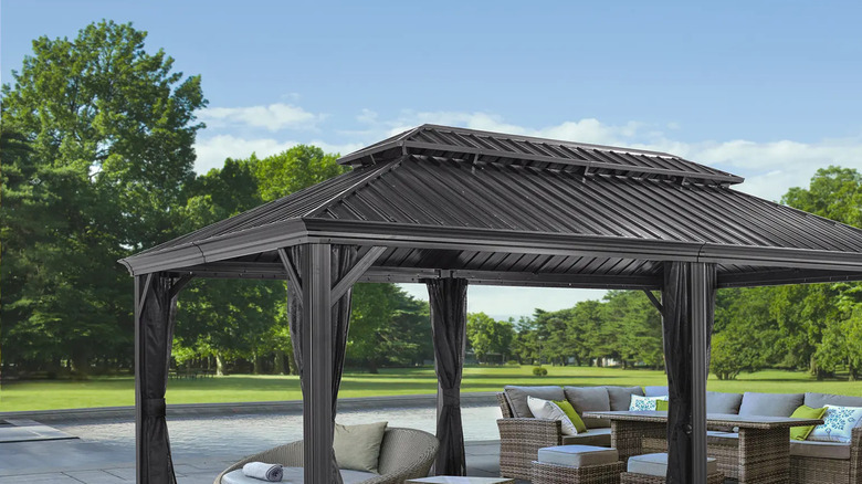 A large garden dining set, stools, plus a lounging chair, all beneath a large steel-roofed gazebo