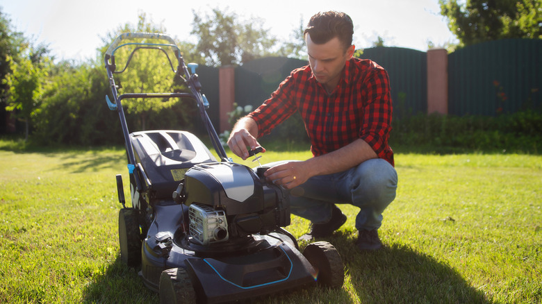 Man standing over lawn mower checking fuel