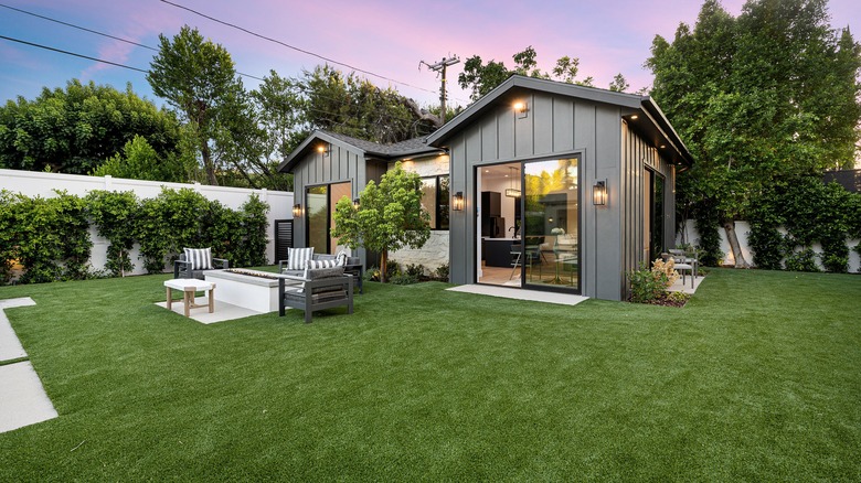 Small grass yard with a tiny house and patio area at sunset.