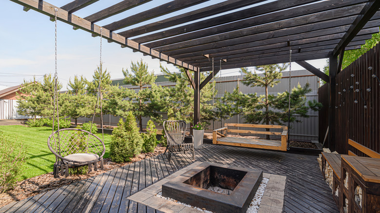 The space under a pergola, including swinging chairs and a fire pit