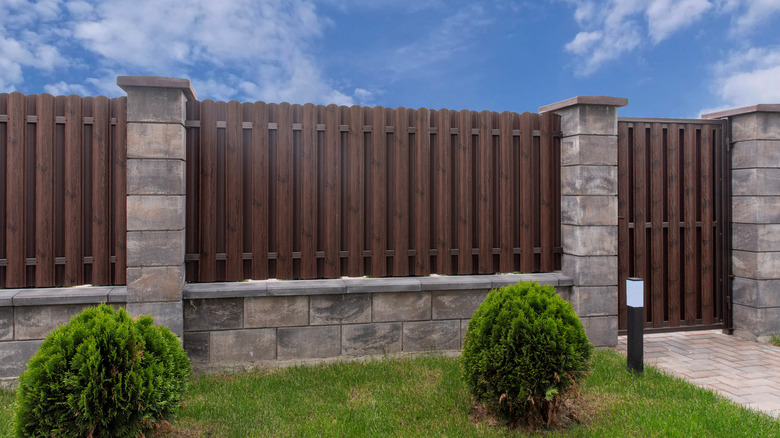 A privacy fence made from wood and stone with sone on the bottom layer and small bushes in front