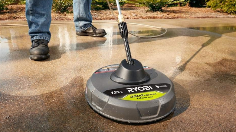 A person wih jeans and work books pressure washing a driveway with the Ryobi surface pressure washer