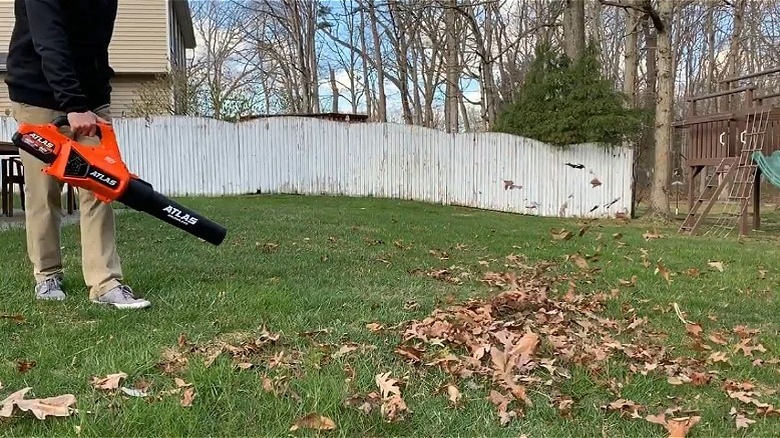 Man in khaki pants and navy sweatshirt blowing leaves in the yard