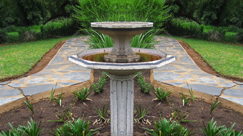 A concrete pedestal birdbath in the center of a lawn
