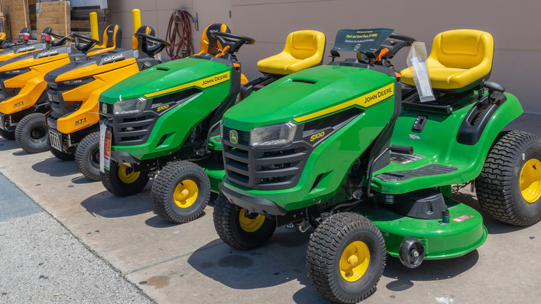 A line-up of John Deer and Cub Cadet riding lawn mowers for sale at a retail store.