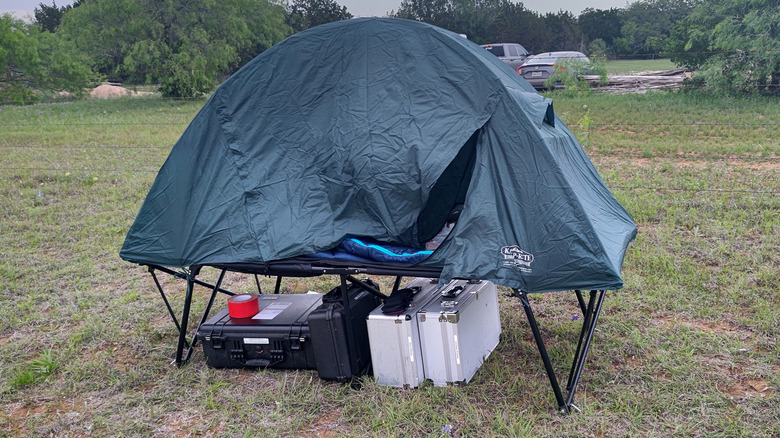 tent cot set up in a field with luggage under it.