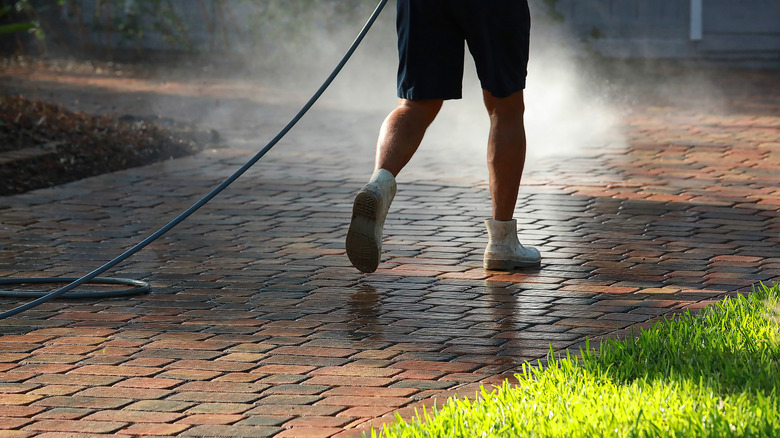 Man hosing off a driveway made of brick pavers