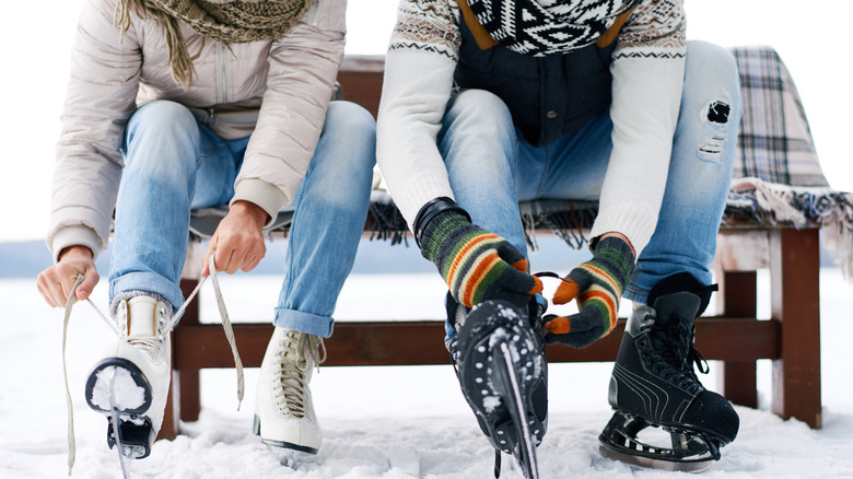Couple tying ice skates outside while sitting on bench