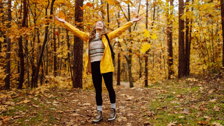 smiling woman in the woods surrounded by autumn foliage