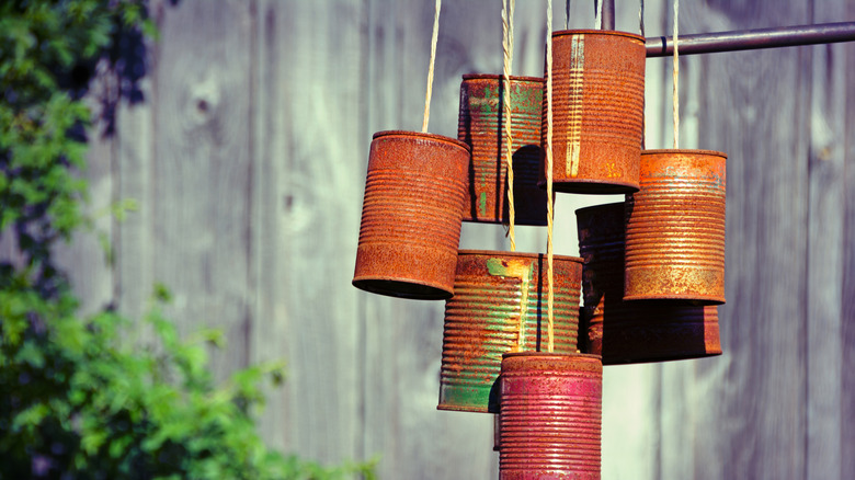 Rusty tin can wind chimes hung from twine in front of wooden fence.