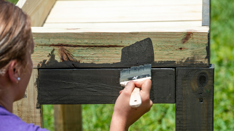 woman adding stain or sealant to an outdoor planter box