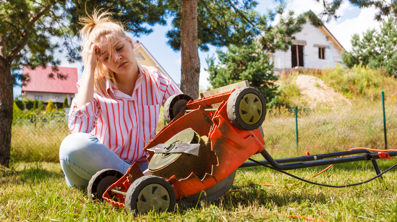 A woman sitting in the grass with broken lawn mower