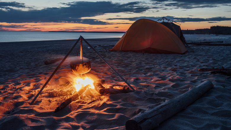 kettle hanging over fire on beach by tent