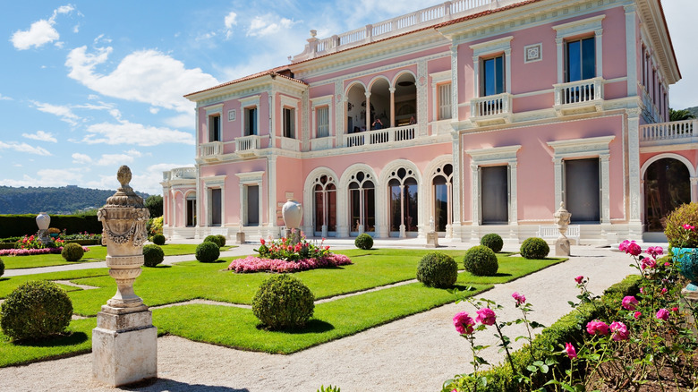 A formal French garden with pink manor house, sculptural elements, round hedges, and rose gardens in France.