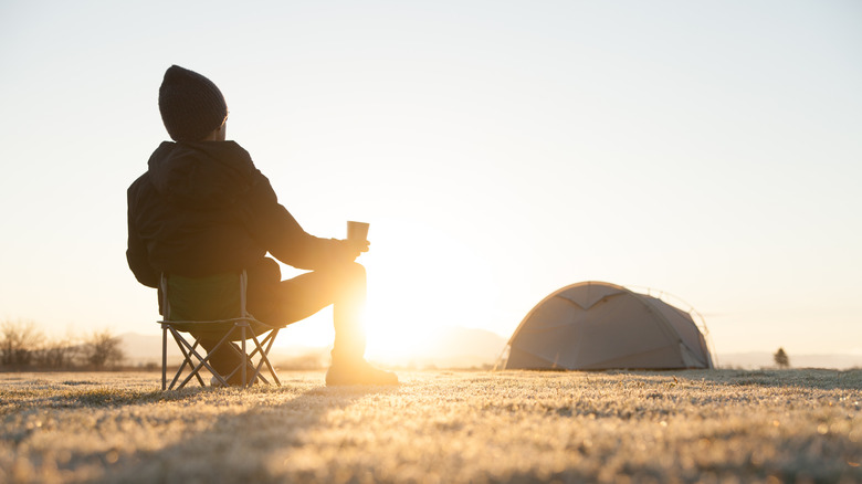 Camper watching sunrise with cup of coffee