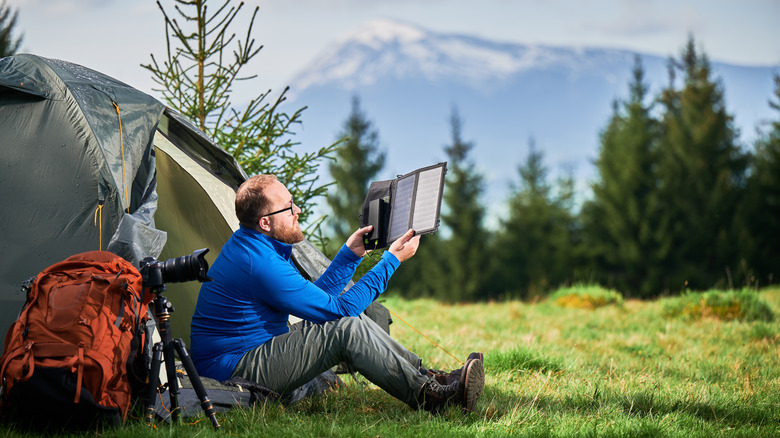 Person outside their tent holding up solar charger