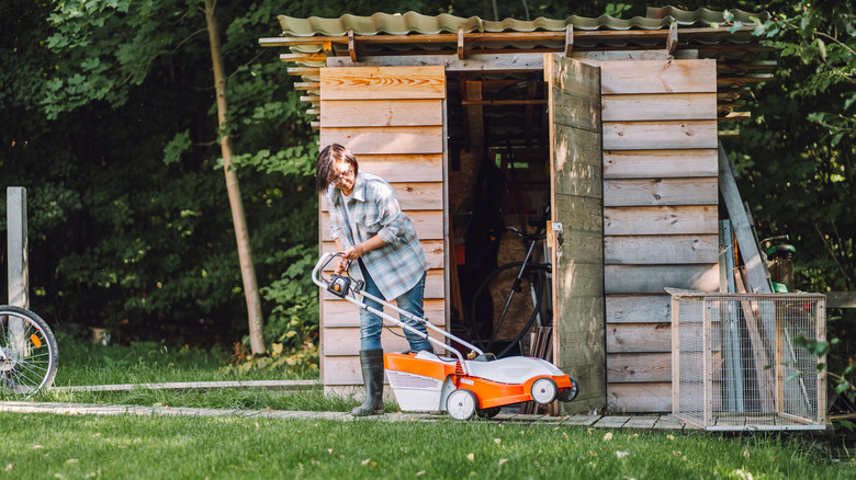 Woman handles an electric mower outside a storage shed