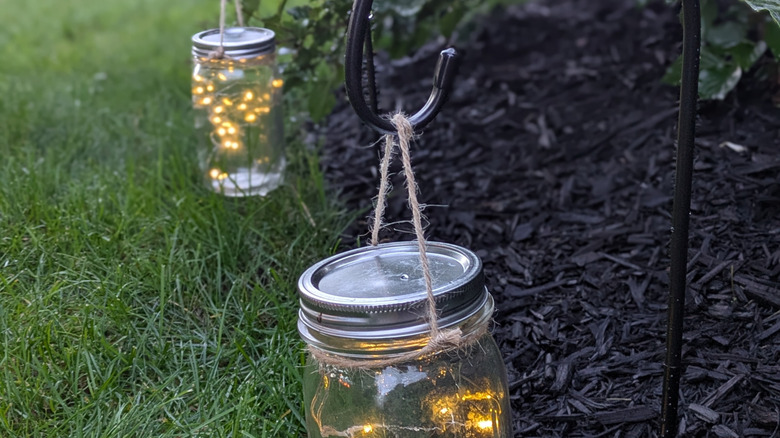 mason jars filled with fairy lights and suspended from shepherd's hooks