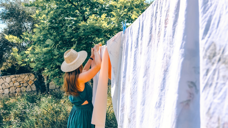 Woman hanging cotton sheets on clothesline in yard