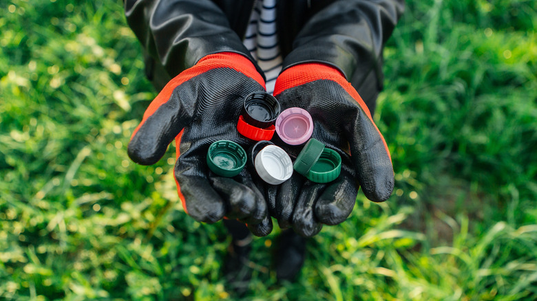 an individual wearing black and red work gloves holding a collection of bottle caps