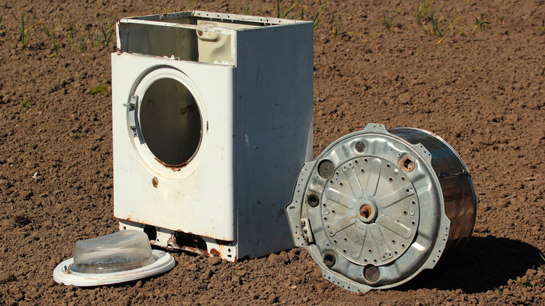 Old washing machine with stainless steel drum outside on dirt