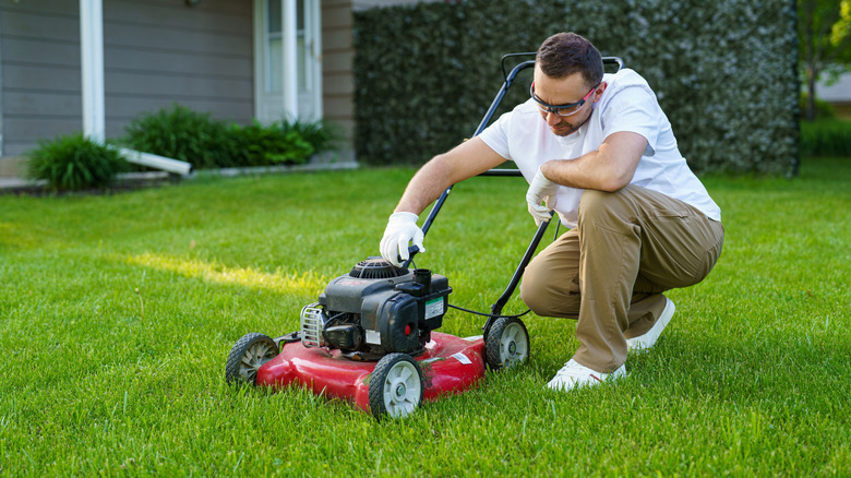 Man examines a red push mower on the lawn
