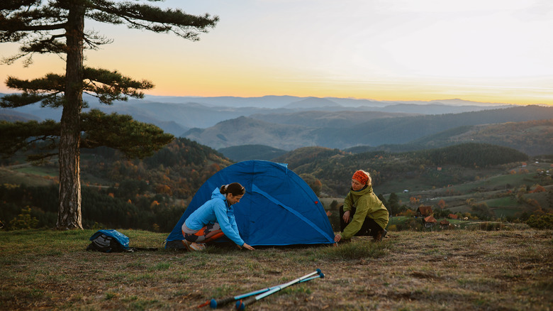 Two women setting up tent on open hilltop