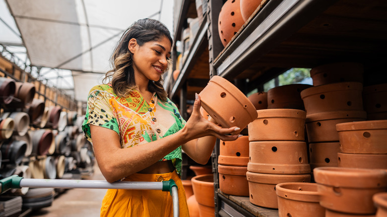 A smiling woman inspecting a clay flower pot at a garden center