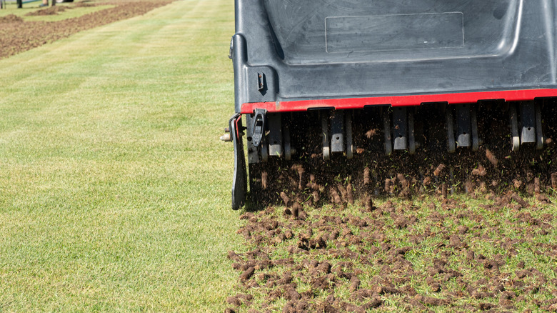 A large mechanical lawn aerator dropping soil plugs on a green lawn.