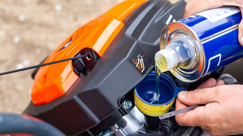 Person adding oil to a mower's engine