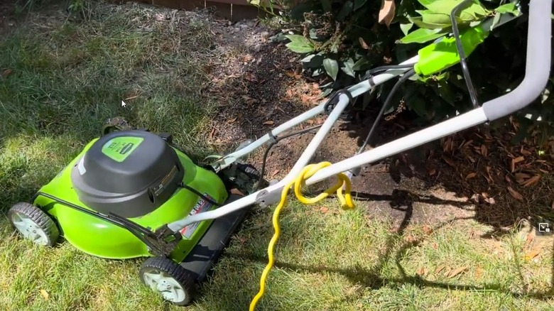 Greenworks 18-inch electric corded mower next to a bush