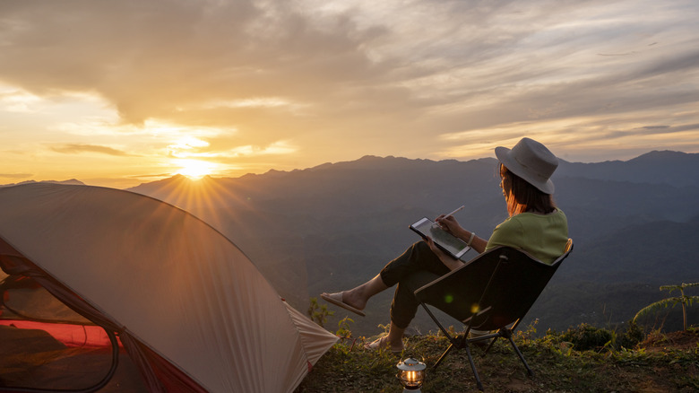 person sitting beside tent looking at sun