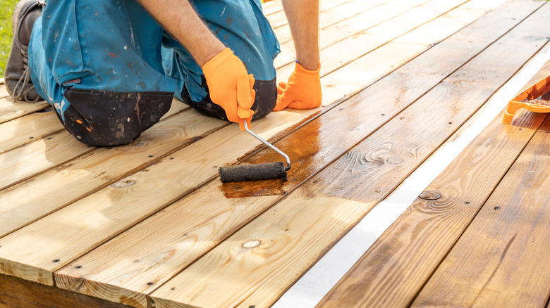 man staining wooden deck by hand showing maintenance needs