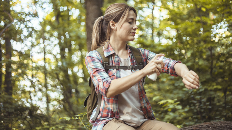 Hiker wearing long-sleeve clothing applying mosquito repellent