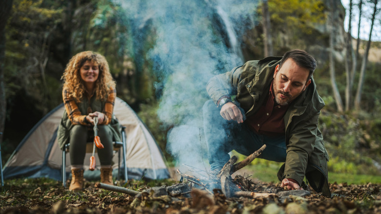 Man adding stick to smoking campfire