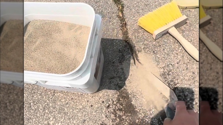 Bucket of polymeric sand with trowel on concrete driveway