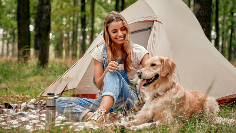 A woman sitting outside a tent in the woods with her dog