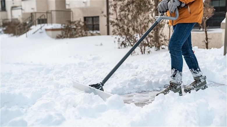Person using snow pusher on driveway