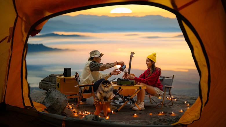 A couple camping with dog, enjoying coffee at sunset