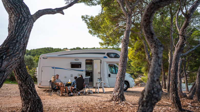 FOur campers sitting outside of their RV at a wooded campsite