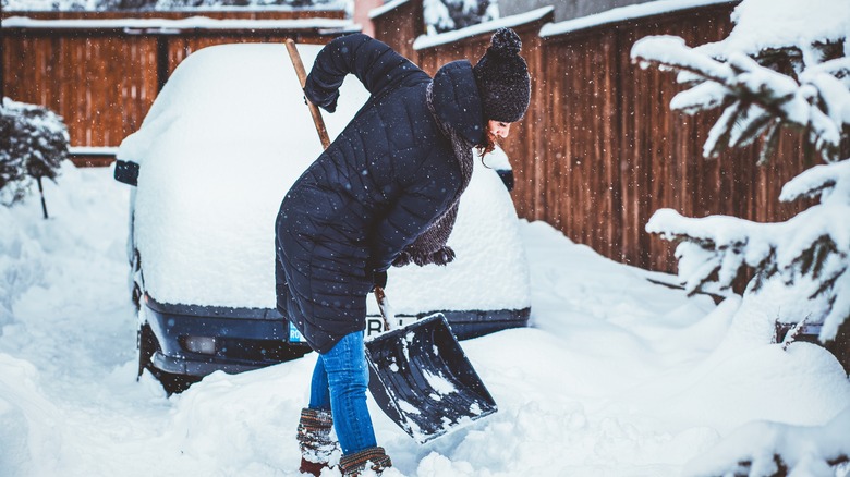A woman with a snow shovel digs her car out of the snow