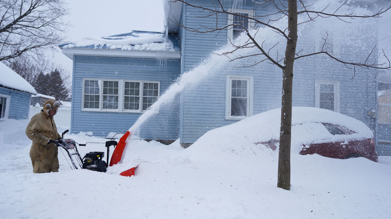 A man pushes a snow blower through thigh-high snowbanks
