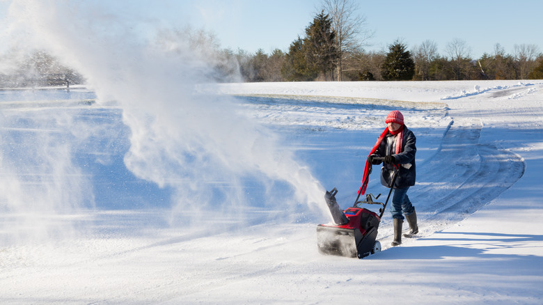 woman uses snow blower to clear driveway