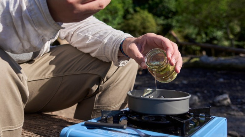 A man pouring oil into a pan on a camp stove
