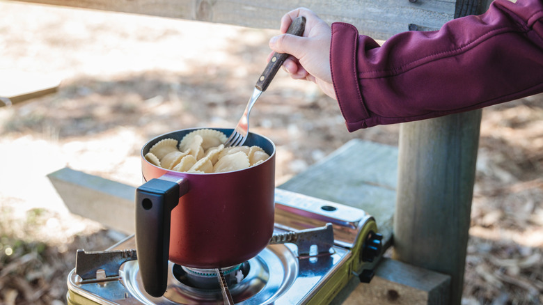 A camper stiring a pot of ravioli on a camp stove