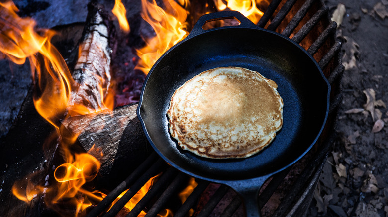 A pancake cooking in a cast iron skillet in a campfire