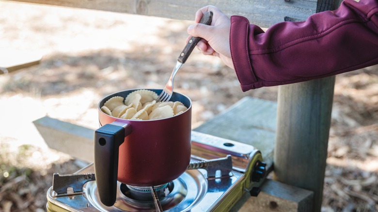 A camper stiring a pot of ravioli on a camp stove